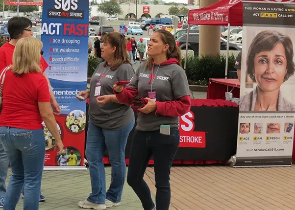 Two women handing out strike out stroke drink koozies