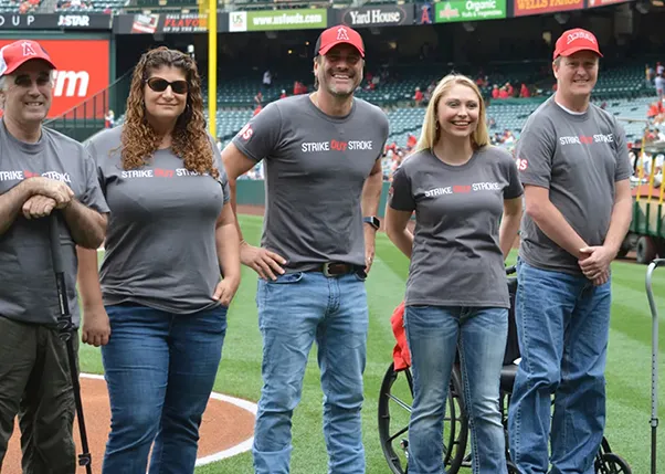 Stroke survivors and event organizers standing on baseball field smiling wearing strike out stroke shirts