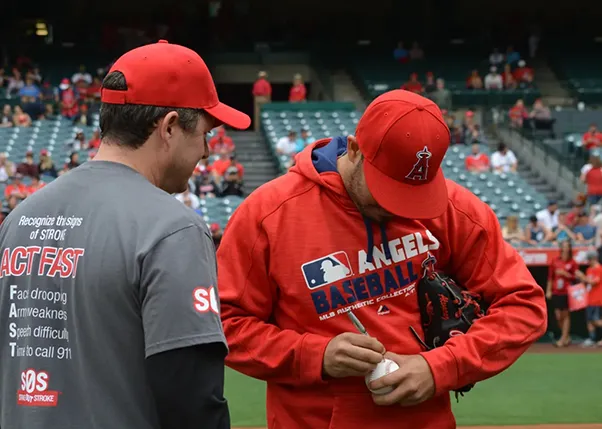 Baseball player signing stroke survivors baseball while standing on the field