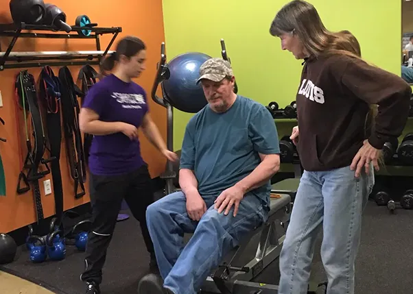 Stroke Survivor Doing Leg Exercises With Personal Trainer and Caregiver